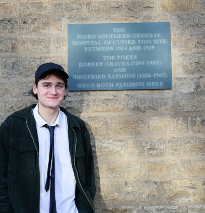 Harry (a young man wearing a tie) with the plaque for Robert Graves and Siegfried Sassoon outside Somerville
